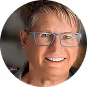 Smiling person with short light brown hair and glasses in natural light.
